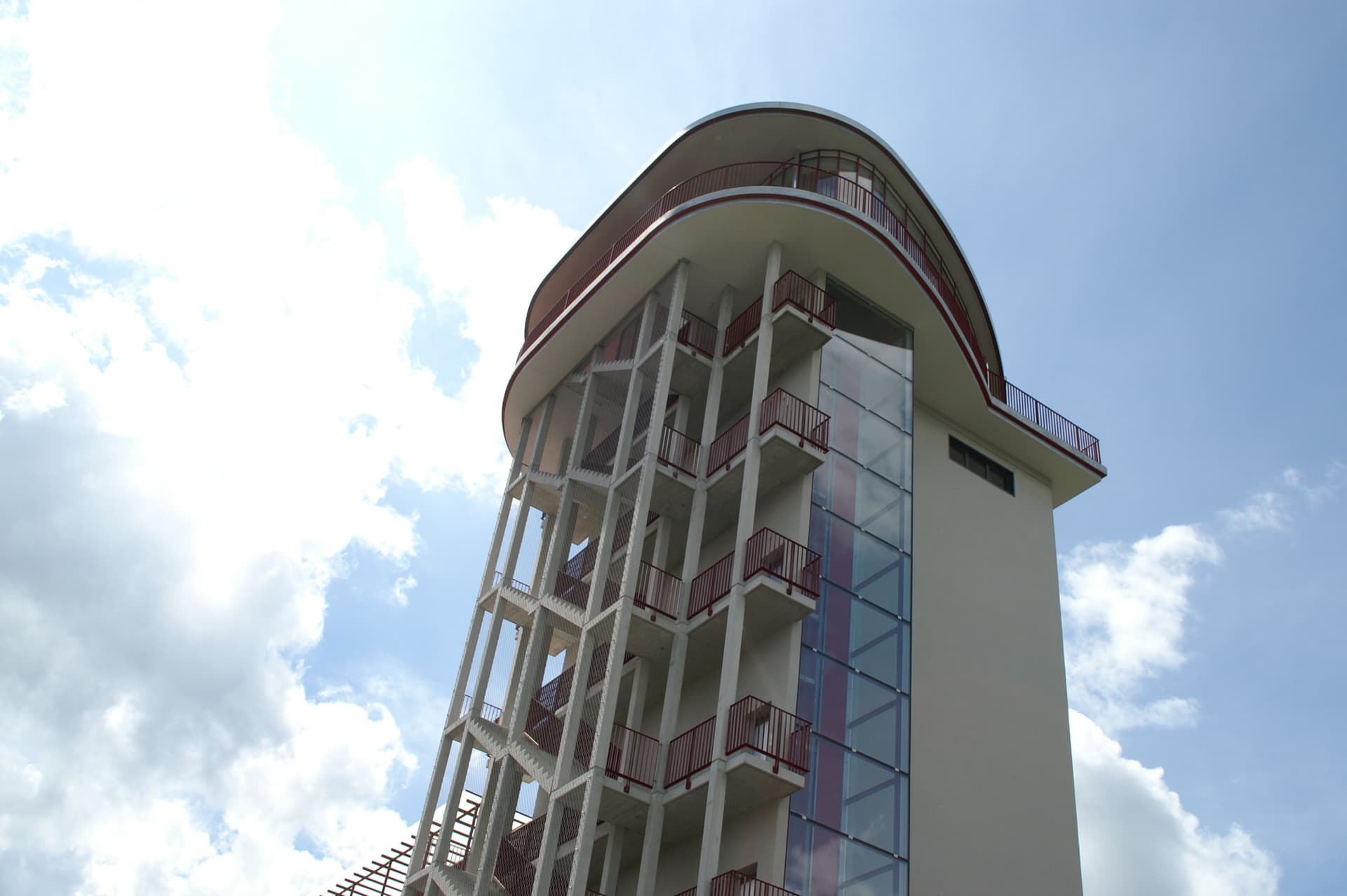 Modernes mehrstöckiges Gebäude mit gebogenem Dach, Glasfassade und offenen Aussentreppen bei sonnigem Himmel