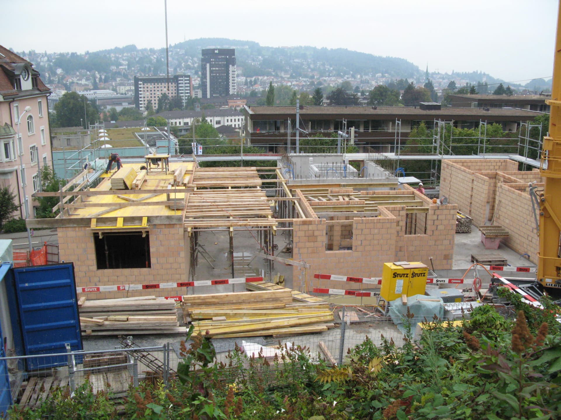 Wohngebäude im Rohbau mit Mauerwerk, Gerüsten, Baumaterial und Arbeitern auf der Baustelle